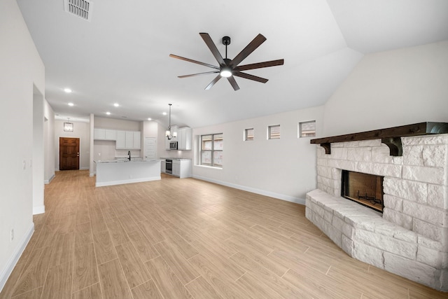 unfurnished living room featuring ceiling fan, sink, a fireplace, and vaulted ceiling