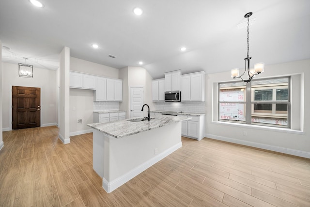 kitchen featuring backsplash, white cabinets, a center island with sink, sink, and decorative light fixtures