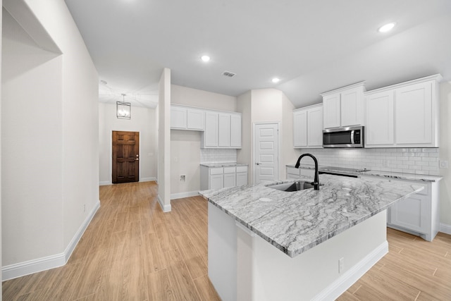 kitchen featuring white cabinets, light stone counters, sink, and an island with sink