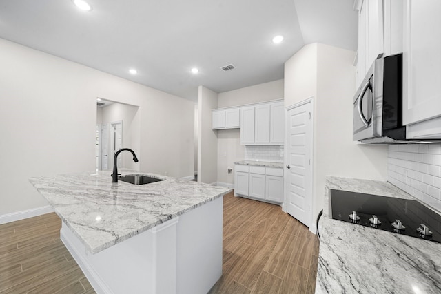 kitchen featuring sink, tasteful backsplash, light stone counters, a center island with sink, and white cabinets