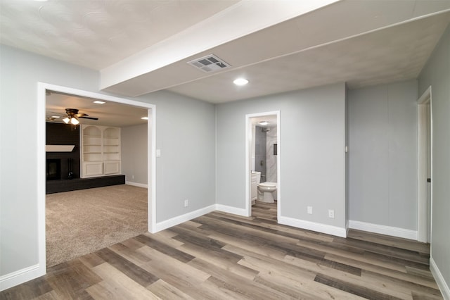 unfurnished room featuring a large fireplace, hardwood / wood-style flooring, built in features, and ceiling fan