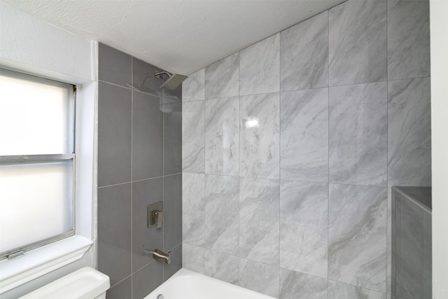 bathroom featuring a textured ceiling, toilet, and tiled shower / bath