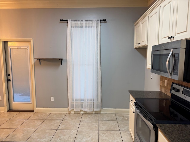 kitchen featuring appliances with stainless steel finishes, dark stone counters, ornamental molding, light tile patterned floors, and white cabinets