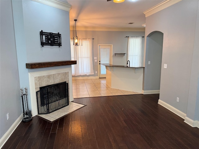 unfurnished living room featuring sink, crown molding, light hardwood / wood-style flooring, a fireplace, and a chandelier