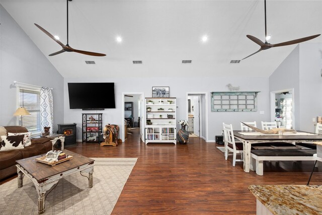 living room with dark hardwood / wood-style flooring, high vaulted ceiling, and a wood stove
