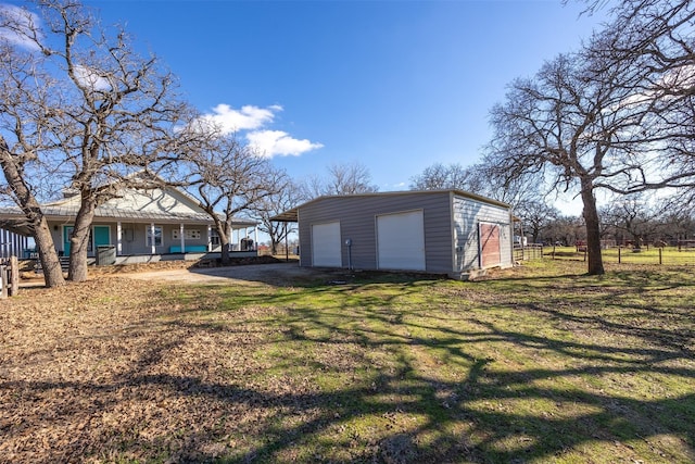 view of yard with covered porch, a garage, and an outbuilding