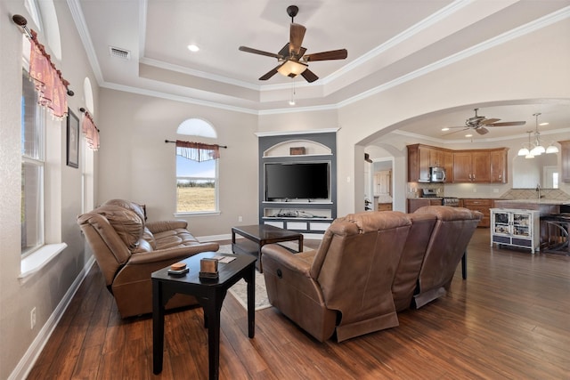 living room with dark hardwood / wood-style flooring, ornamental molding, ceiling fan with notable chandelier, a tray ceiling, and sink