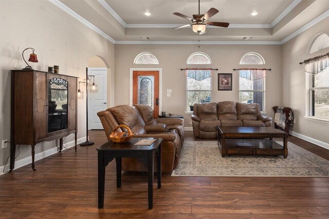 living room with a raised ceiling, ceiling fan, crown molding, and dark wood-type flooring