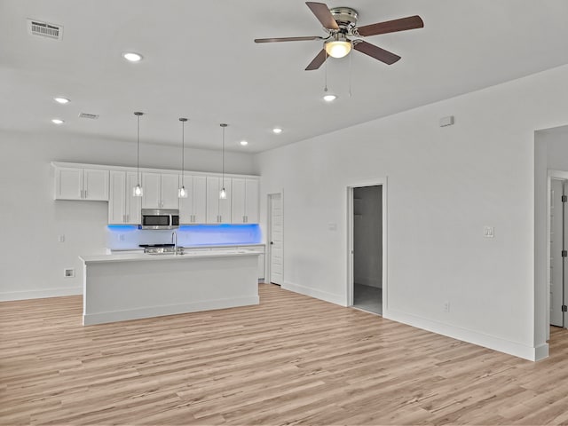 217 Rosemary Dr, Azle, TX 76020 - kitchen featuring stainless steel microwave, light wood-type flooring, light countertops, a center island with sink, and baseboards