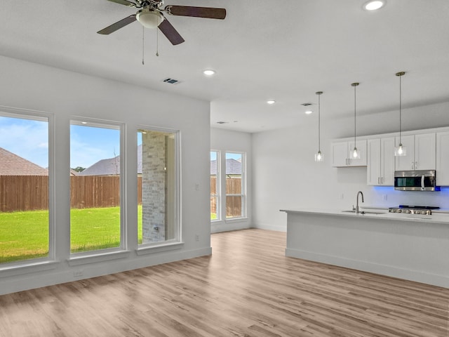 217 Rosemary Dr, Azle, TX 76020 - kitchen with stainless steel microwave, a sink, white cabinets, light wood-type flooring, and hanging light fixtures