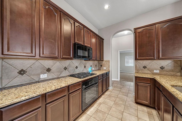 kitchen with light stone counters, arched walkways, light tile patterned floors, backsplash, and black appliances