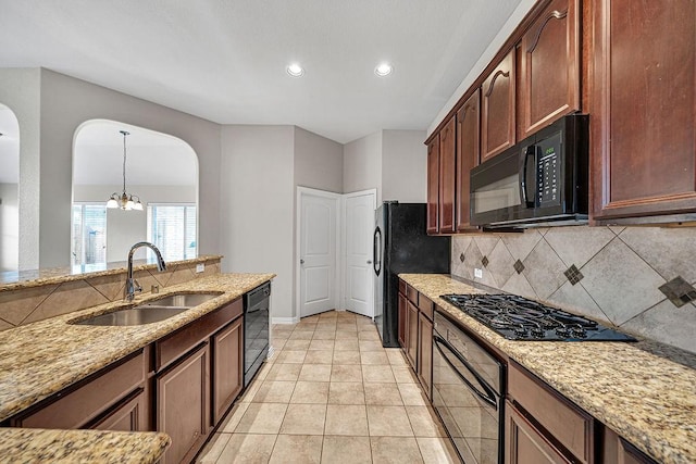 kitchen with light stone counters, a sink, black appliances, tasteful backsplash, and pendant lighting