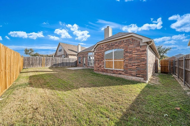 back of property with brick siding, a lawn, a chimney, and a fenced backyard