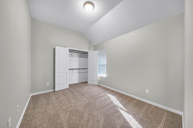 unfurnished bedroom with lofted ceiling, a textured ceiling, carpet flooring, baseboards, and a closet