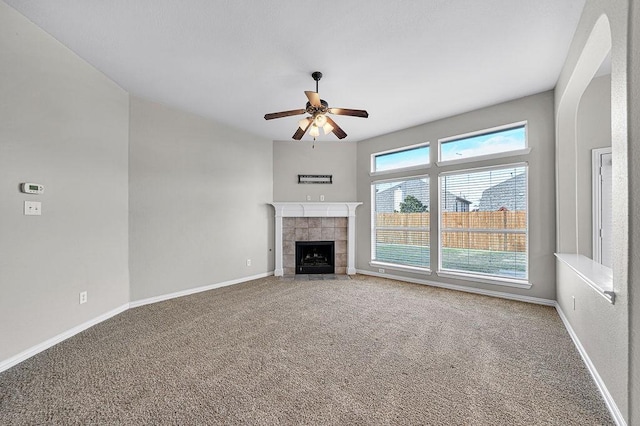 unfurnished living room featuring ceiling fan, carpet floors, a tiled fireplace, and baseboards