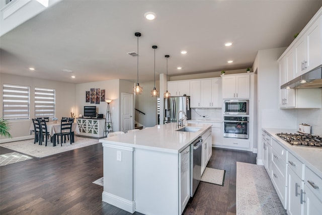 kitchen with white cabinetry, sink, hanging light fixtures, stainless steel appliances, and a kitchen island with sink