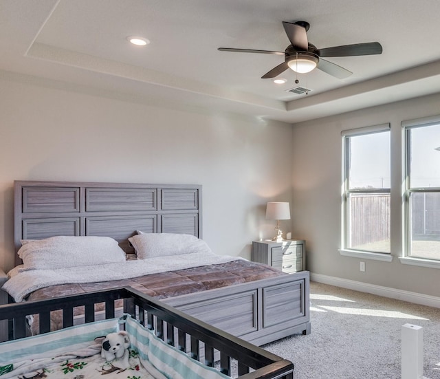 carpeted bedroom with a tray ceiling, multiple windows, and ceiling fan