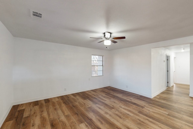 empty room featuring ceiling fan, wood finished floors, visible vents, and baseboards