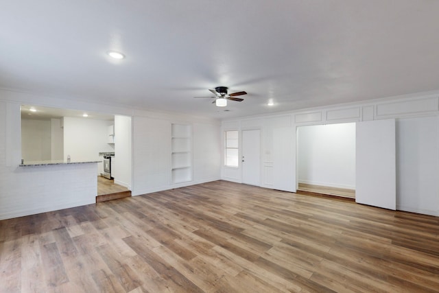 unfurnished living room featuring light wood finished floors, ceiling fan, built in shelves, and crown molding