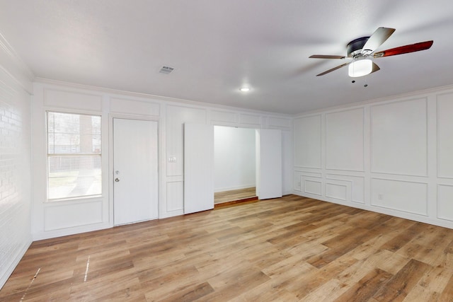 interior space featuring crown molding, a ceiling fan, light wood-style flooring, and a decorative wall