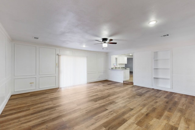 unfurnished living room featuring built in shelves, wood finished floors, visible vents, and a decorative wall