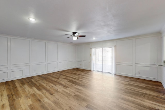 spare room with a ceiling fan, a decorative wall, and wood finished floors