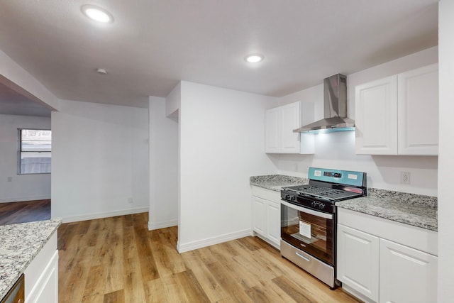 kitchen with light stone countertops, wall chimney range hood, stainless steel gas range, and white cabinets