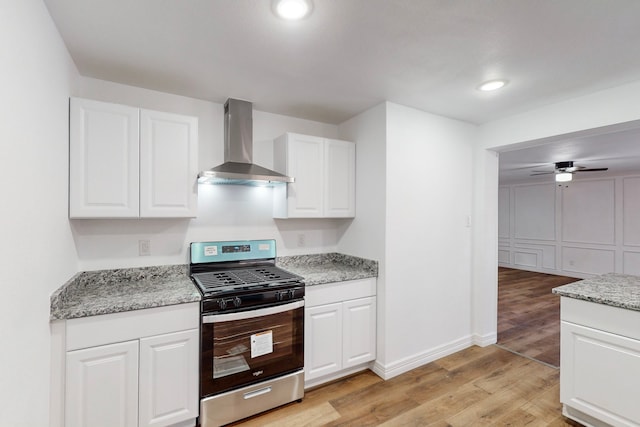 kitchen featuring light wood finished floors, white cabinetry, light stone countertops, stainless steel gas range oven, and wall chimney exhaust hood