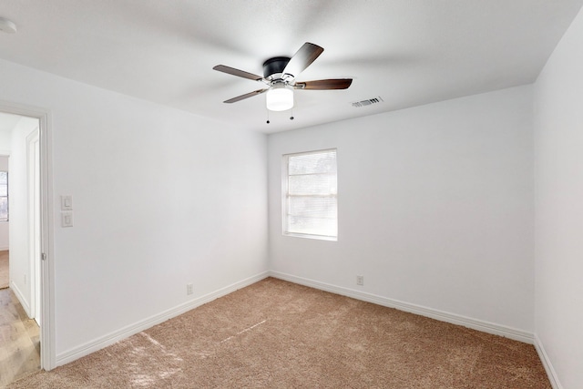 empty room featuring a ceiling fan, light colored carpet, visible vents, and baseboards