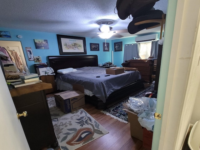 bedroom featuring an AC wall unit, ceiling fan, a textured ceiling, and hardwood / wood-style flooring