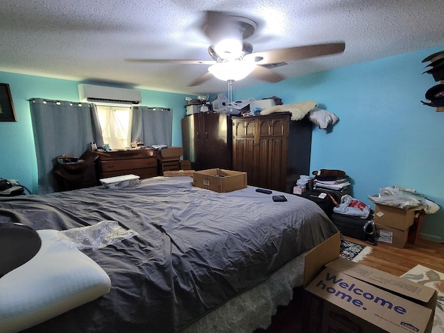 bedroom featuring a textured ceiling, hardwood / wood-style flooring, a wall mounted AC, and ceiling fan