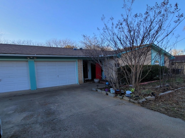 single story home featuring a garage, brick siding, driveway, and roof with shingles