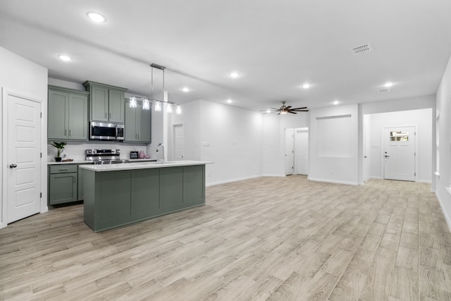 kitchen featuring a center island with sink, light wood-type flooring, pendant lighting, ceiling fan, and stainless steel appliances