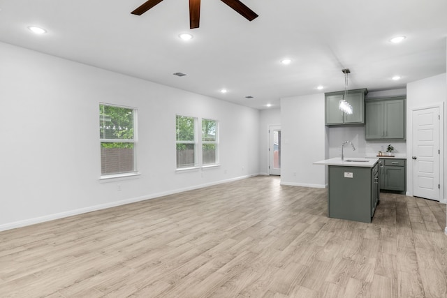 kitchen with sink, a center island with sink, light wood-type flooring, pendant lighting, and ceiling fan