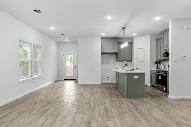 kitchen with sink, hanging light fixtures, a kitchen island with sink, light hardwood / wood-style floors, and stainless steel appliances