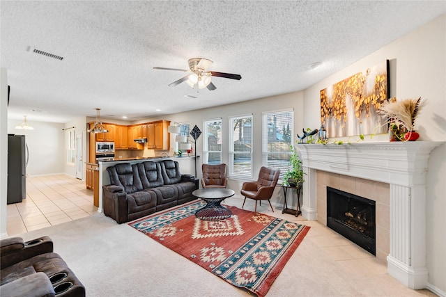 tiled living room featuring a textured ceiling, ceiling fan, and a tiled fireplace