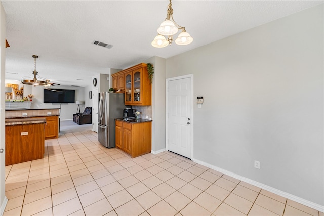 kitchen with pendant lighting, backsplash, ceiling fan with notable chandelier, stainless steel fridge, and light tile patterned floors