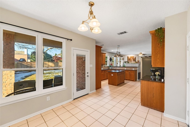 kitchen featuring ceiling fan with notable chandelier, hanging light fixtures, light tile patterned floors, a textured ceiling, and a kitchen island