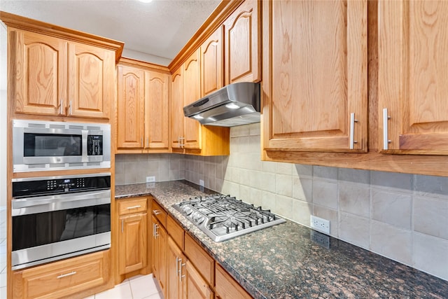 kitchen with decorative backsplash, light tile patterned flooring, appliances with stainless steel finishes, and dark stone counters