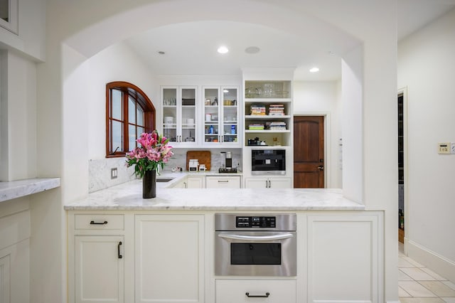 kitchen featuring white cabinets, light tile patterned flooring, light stone counters, and stainless steel oven