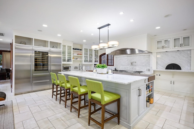 kitchen featuring appliances with stainless steel finishes, a center island with sink, white cabinets, hanging light fixtures, and a breakfast bar area