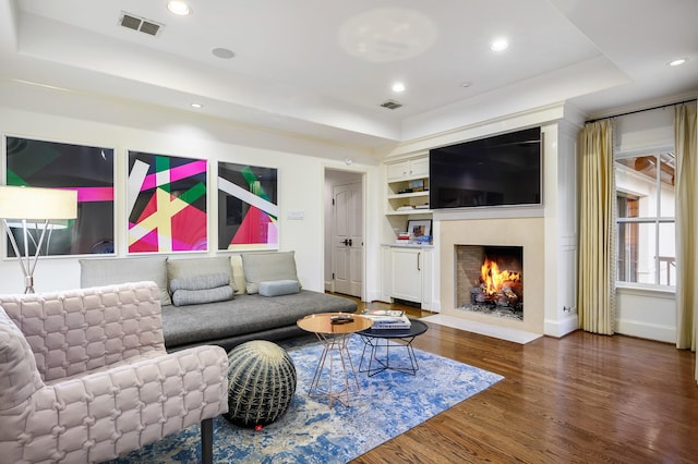 living room featuring a raised ceiling, built in shelves, and hardwood / wood-style flooring