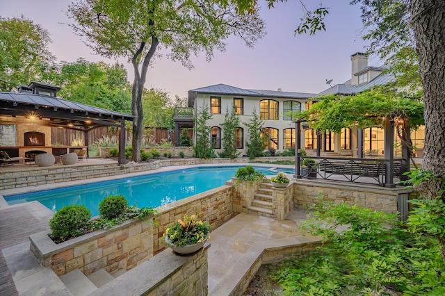 pool at dusk featuring a gazebo, a patio area, and an outdoor fireplace