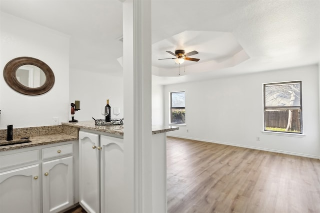 kitchen with a raised ceiling, light stone counters, white cabinetry, light wood-style floors, and baseboards