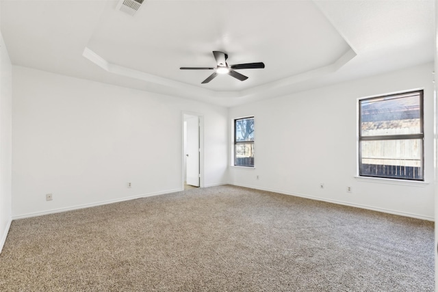 spare room featuring carpet, baseboards, visible vents, a ceiling fan, and a tray ceiling