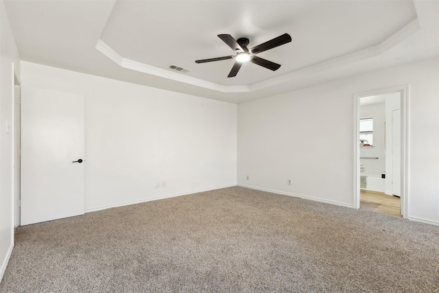 carpeted spare room with visible vents, a raised ceiling, baseboards, and ceiling fan