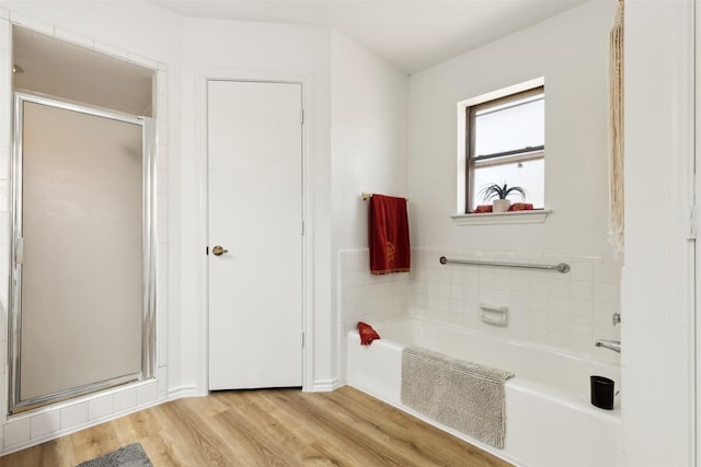 full bathroom featuring a bath, a shower stall, and wood finished floors