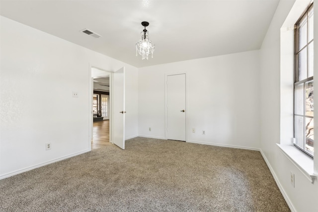 carpeted empty room with an inviting chandelier, visible vents, and baseboards