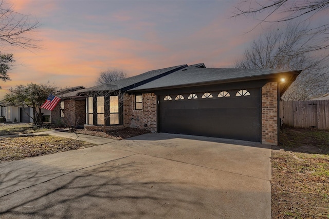 view of front facade featuring brick siding, an attached garage, driveway, and fence