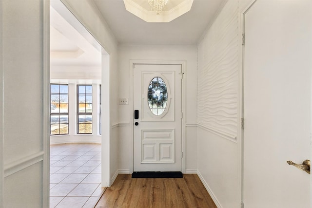 entryway with a raised ceiling, crown molding, light wood-type flooring, and baseboards